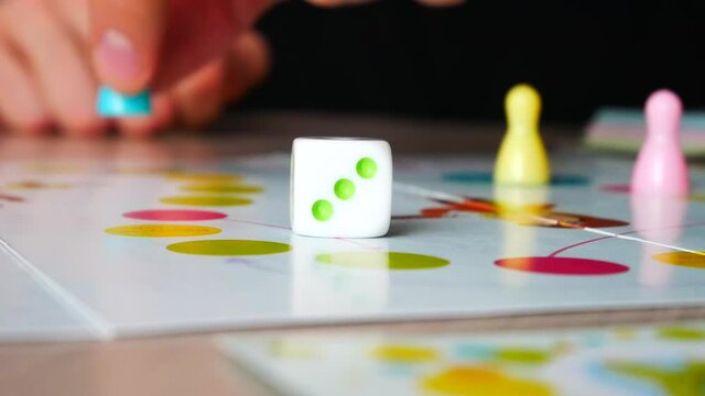 A man rolls a dice and moves a piece playing a board game