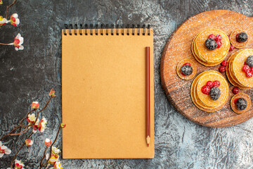 Classic American pancakes on wooden cutting board with flowers and notebook on gray background