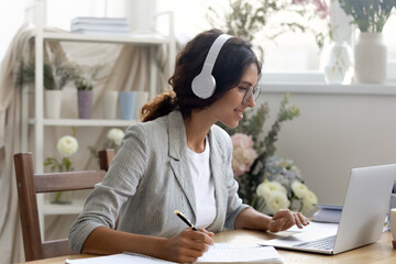Interested millennial woman enterpreneur wearing earphones studying foreign language via web app....