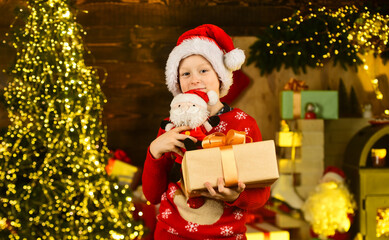 Fototapeta na wymiar Real happiness. Child happy excited near christmas tree. Merry christmas. Happy childhood concept. Kid wear santa hat and christmas sweater. Santa brought me gifts. December tradition. Sale discount