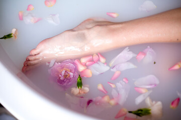 Obraz na płótnie Canvas A girl's foot in a bathtub filled with milk and rose petals.Relax, romance