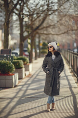 Fototapeta premium Elegant girl walk in a winter city. Woman in a white knited sweater. Beautiful lady with dark hair.