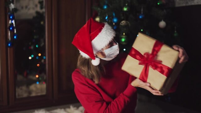 girl in red clothes and medical mask unfold New year gifts. the concept of celebrating Christmas midnight. Holiday's decor boce, Christmas tree