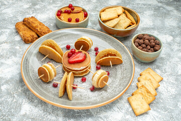 Top view of pancake decoration with fruits and biscuits on a white plate and white background