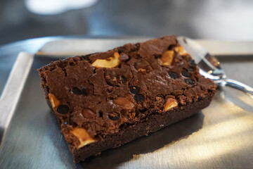 Fototapeta na wymiar Close up piece of Chocolate fudge brownie with cocoa chips and cashew nuts on aluminium plate