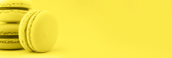 Three macaroons on Illuminating Yellow color of the year 2021 background. Macro banner concept, copy space.