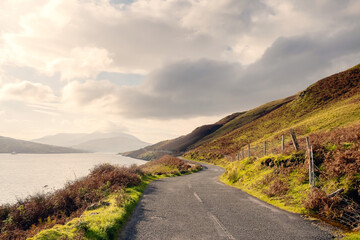 Small asphalt road with beautiful scenery, Killary fjord, Connemara, West of Ireland. Travel and transportation concept. Warm sunny day, Cloudy sky. Nobody