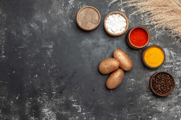 Horizontal view of variety of spices and potatoes on dark background