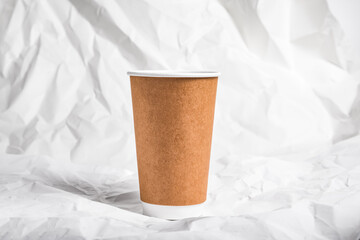 Brown paper disposable coffee mug, cup on crumpled background