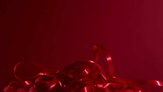 Deep ruby colored curly silky ribbons are dropping down on a velvety cherry red backdrop. Atmospheric video background. New year, Christmas, st Valentine festive mood 4k high quality video footage