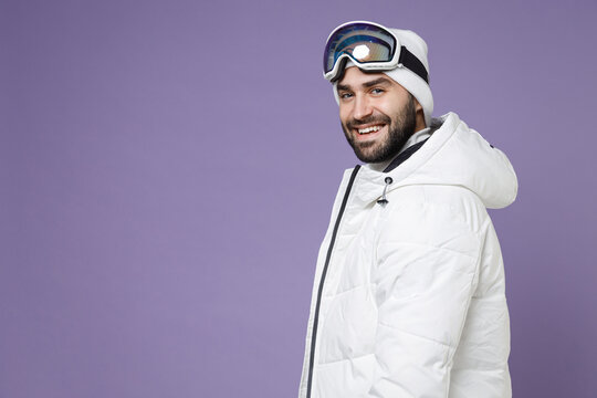 Side view cheerful skier man in white windbreaker jacket ski goggles mask looking camera spend extreme weekend winter season in mountains isolated on purple background. People lifestyle hobby concept.