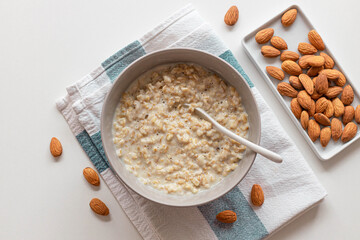 Top view of homemade oatmeal porridge with nut almonds in bowl, ceramic spoon on white background. Health breakfast food concept. Copy space.