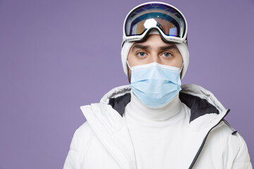Fototapeta na wymiar Skier man in warm white windbreaker jacket ski goggles face mask to safe from coronavirus virus covid-19 spend extreme weekend winter in mountains isolated on purple background. People hobby concept.