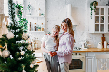 mother and daughter in the kitchen decorated for Christmas and new year, drinking tea or cocoa, conversation, waiting for guests