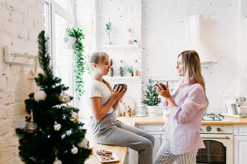 mother and daughter in the kitchen decorated for Christmas and new year, drinking tea or cocoa, conversation, waiting for guests