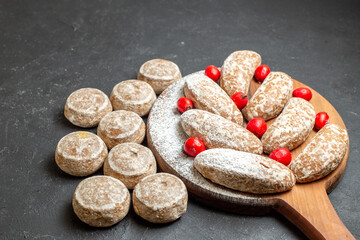 Delicious cookies on a brown cutting board with red cornell berries on dark background