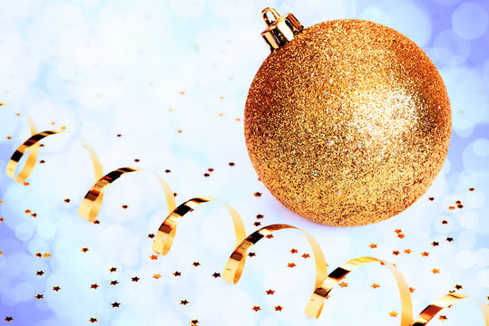 Golden Christmas Ball, Gold Streamer And Stars On Light Blue Background With Defocused Lights. Xmas Card. New Year Concept.