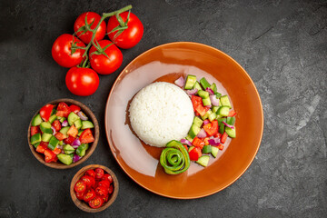 Horizontal view of different kinds of vegetables and rice meal on a brown plate on dark background