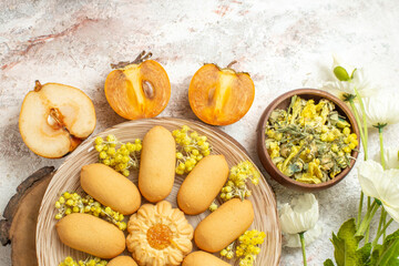 a plate of cookie on wooden plate and a bowl of herb and fruits and white flowers on marble ground