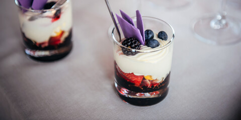 Delicious dessert of whipped cream and fresh berries in glass with spoon. Portioned sweet snacks in restaurant at festive banquet. Blackberries, blueberries, strawberries, berry topping, butter cream.