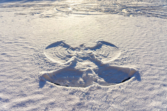 print of a snow angel on fresh white snow and frozen lake at sunset. Abstract background, Christmas, twinter fun, snowy