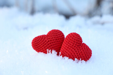 Fototapeta premium Valentine's hearts on a snow in winter forest. Two red knitted symbols of love, background for romantic greeting card
