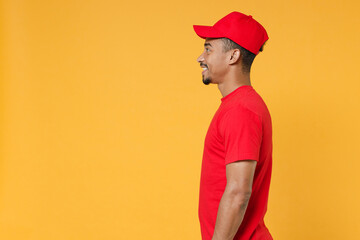 Side view delivery employee african man in red cap blank t-shirt uniform workwear work courier dealer service during quarantine coronavirus covid-19 virus concept isolated on yellow background studio.