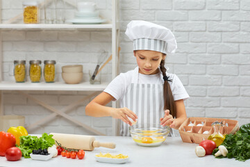 cute little girl in chef hat and an apron is breaking yellow egg into fresh dough in the kitchen. child cooking with dough