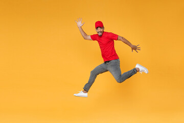 Fototapeta na wymiar Full length fun delivery employee african man in red cap blank print t-shirt uniform workwear work courier dealer service on covid-19 virus concept jump run walk isolated on yellow background studio.