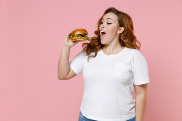 Excited young redhead plus size body positive woman 20s in white casual t-shirt hold eating...