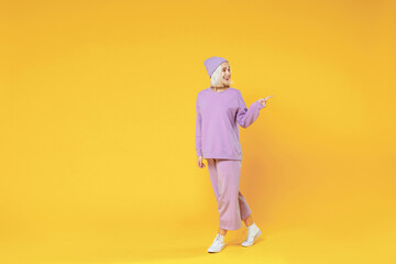 Fototapeta na wymiar Full length of young caucasian woman 20s bob haircut wearing casual basic purple suit beanie hat pointing index fingers aside on copy space looking away isolated on yellow background studio portrait.