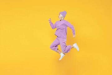 Fototapeta na wymiar Full length of young energetic caucasian excited fun woman 20s wearing casual basic purple suit beanie hat side profile view running jumping isolated on yellow color background studio portrait