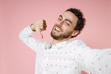 Close up of funny young bearded man 20s in casual white shirt standing doing selfie shot on mobile phone pointing thumb on himself looking camera isolated on pastel pink background studio portrait.