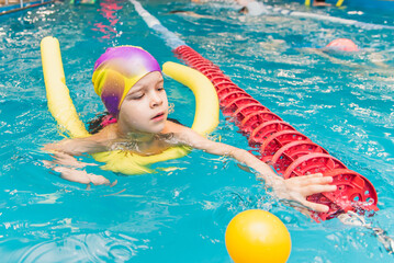 A little boy with a life jacket on his chest learns to swim in an indoor pool.