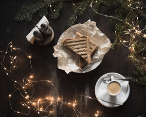 Sandwich and espresso surrounded by New Year's lights and pine branches. Food dark background. Christmas lunch in a cafe