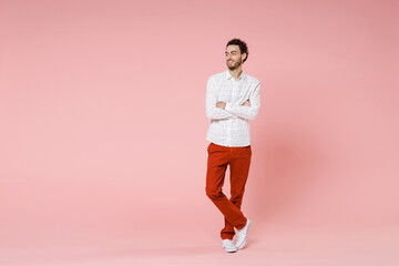Fototapeta na wymiar Full length of smiling attractive young bearded man 20s wearing basic casual white shirt standing holding hands crossed looking aside isolated on pastel pink color wall background studio portrait.