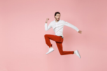 Fototapeta na wymiar Full length side view of shocked young bearded man 20s wearing basic casual white shirt jumping like running spreading hands looking camera isolated on pastel pink color background studio portrait.