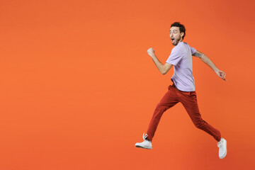 Full length of shocked amazed young bearded man 20s wearing casual violet t-shirt jumping like running keeping mouth open looking aside isolated on bright orange color wall background studio portrait.