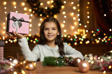 cute happy little child girl holding Christmas gift box in hand at home.