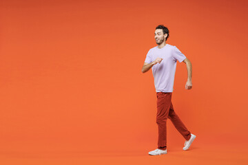 Full length side view of excited cheerful funny young bearded man 20s wearing basic casual violet t-shirt walking going looking aside isolated on bright orange color wall background studio portrait.