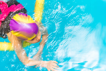 A little boy with a life jacket on his chest learns to swim in an indoor pool.