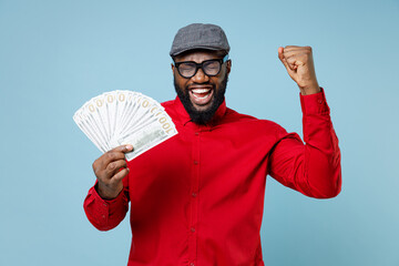 Joyful young bearded african american man 20s in casual red shirt eyeglasses cap hold fan of cash...