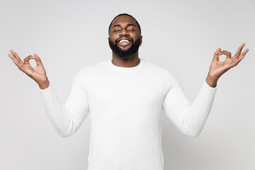Smiling young african american man 20s wearing casual basic sweater standing hold hands in yoga gesture relaxing meditating trying to calm down isolated on white color wall background studio portrait.
