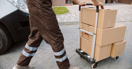 Close up of young Caucasian delivery man taking box from van standing on street putting parcels on...
