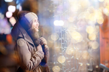 happy girl lights evening christmas shopping standing on the street by the shop window