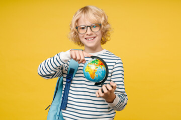Smiling male kid teen boy 10s years old in striped sweatshirt glasses backpack point index finger on world Earth globe isolated on yellow color background, child studio portrait. Education concept.