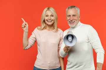 Excited couple two friends elderly gray-haired man blonde woman in white pink casual clothes screaming in megaphone pointing index finger aside up isolated on orange color background studio portrait.