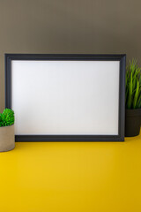 Black landscape frame mockup on easel beside a small houseplant, workspace decoration in minimal concept.