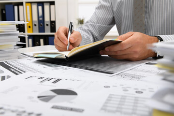 business concept - businessman working in office, table and workspace close view, checks financial reports, writes and counts