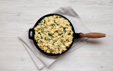 Homemade Spinach Mac and Cheese in a cast-iron pan on a white wooden background, top view. Flat lay, overhead, from above.
